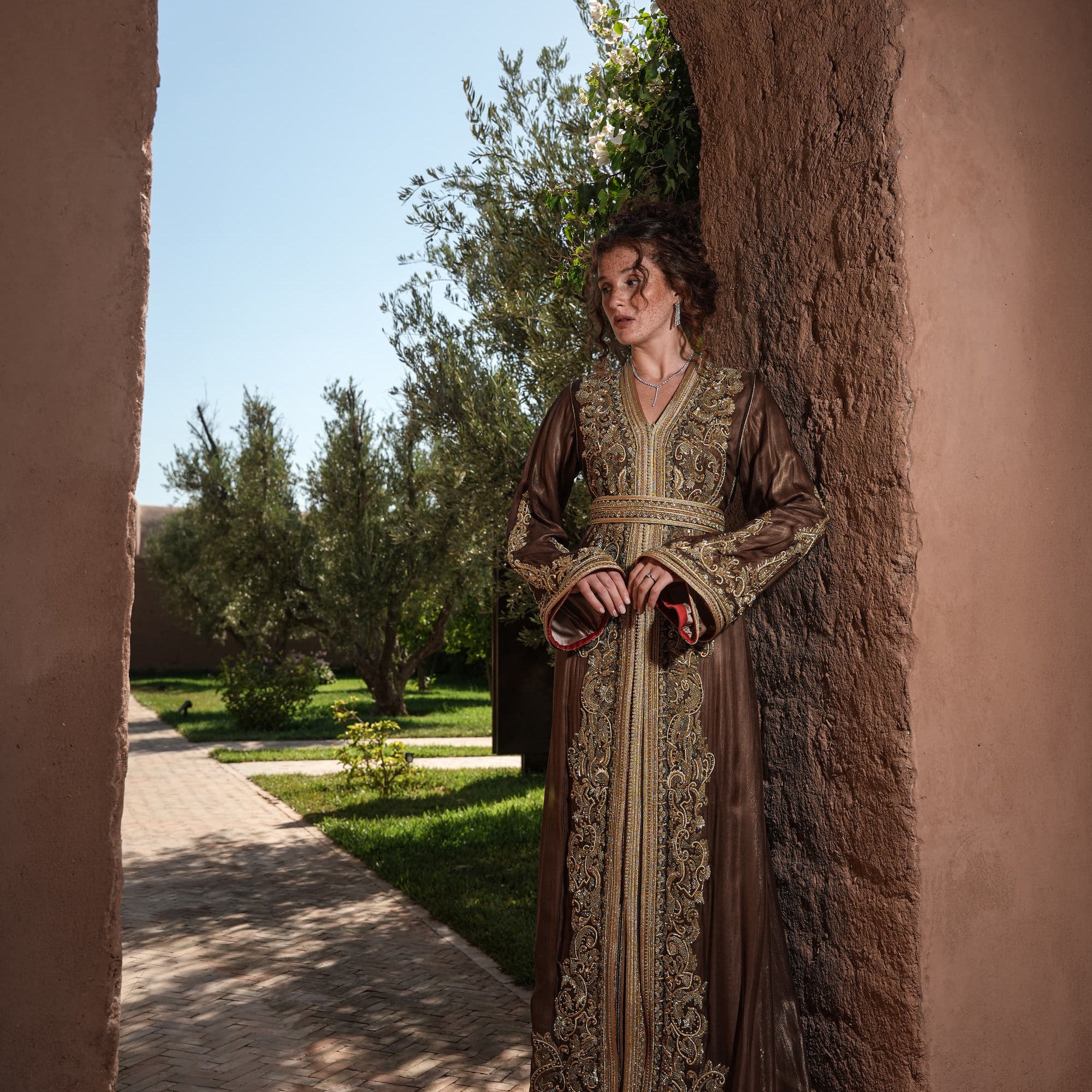 Bronze Reverie lamé organza Moroccan kaftan with gold embroidery, worn open over a champagne dress, full-length view