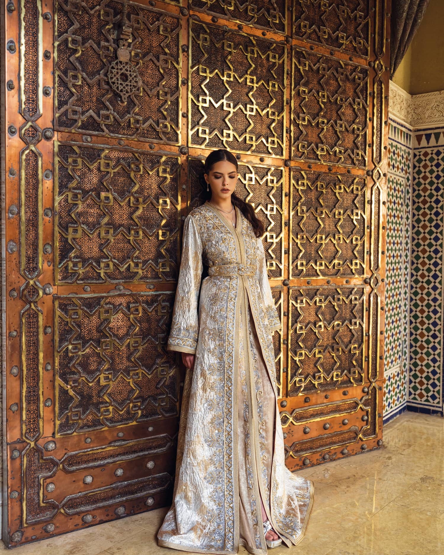 Ivory gold Moroccan kaftan with ornate embroidery before carved door