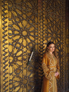 Bronze Moroccan caftan beside ornate golden door with green embroidery accents