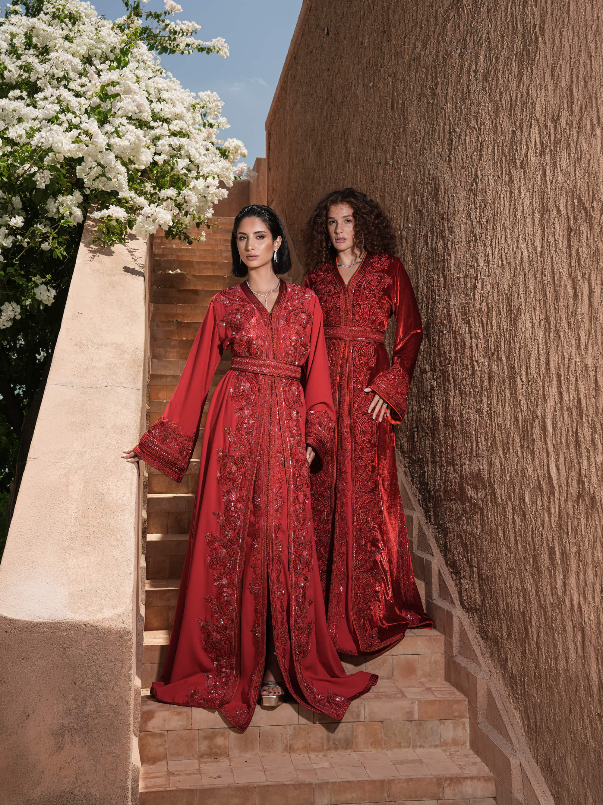 Carmine Cadence red crepe Moroccan kaftan with sequined paisley embroidery, braided belt and flared sleeves, shown alongside a second look