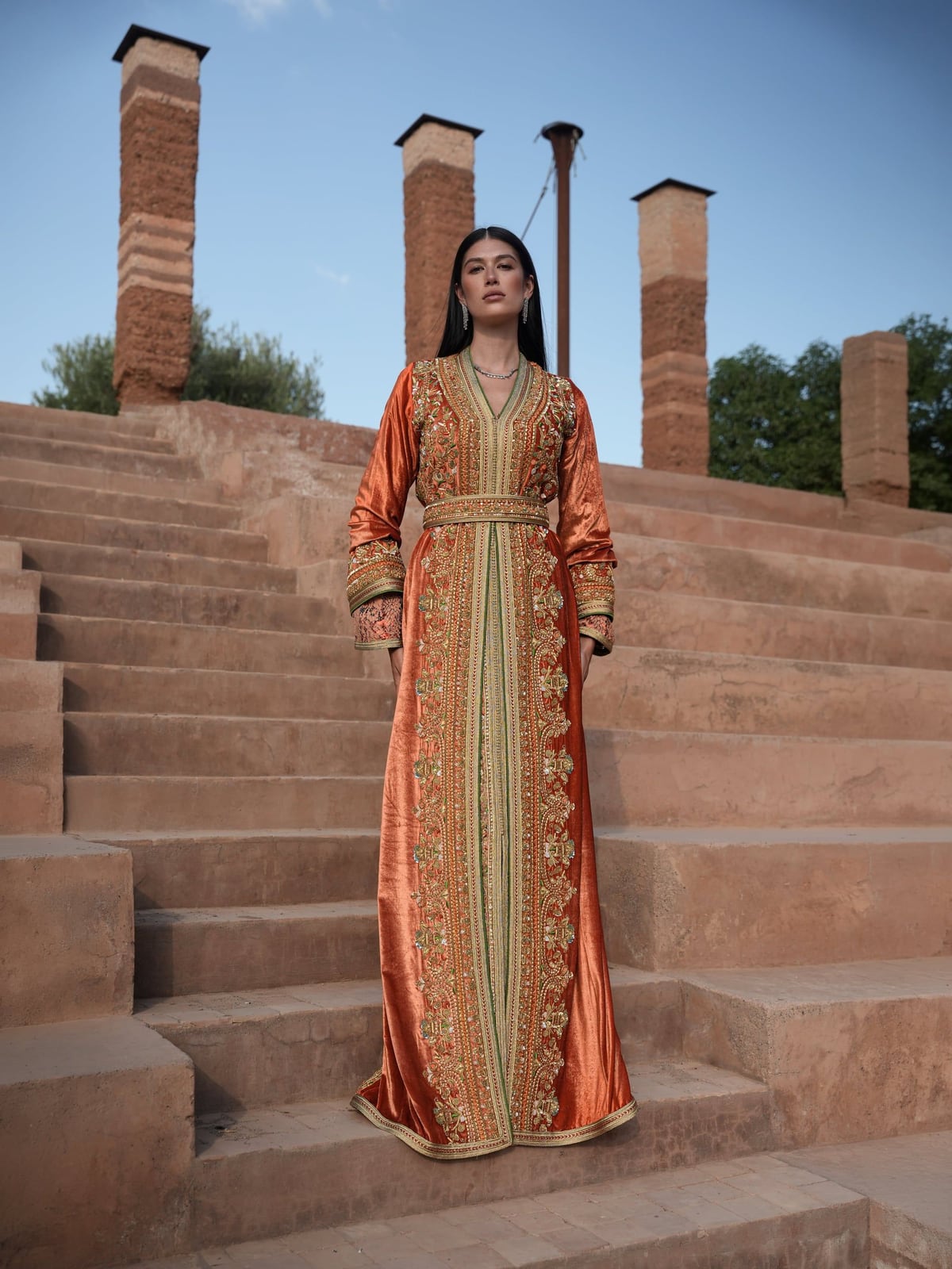 Terracotta Zenith rust Moroccan kaftan with gold embroidery on riad steps