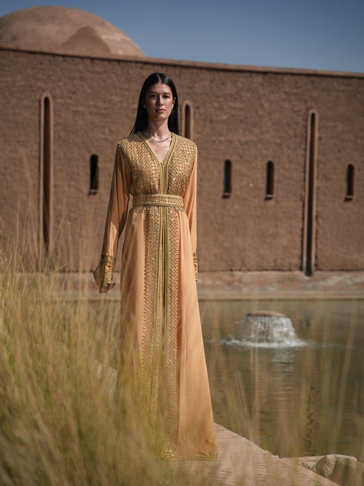 Amber Vigil gold Moroccan kaftan beside a Marrakech fountain