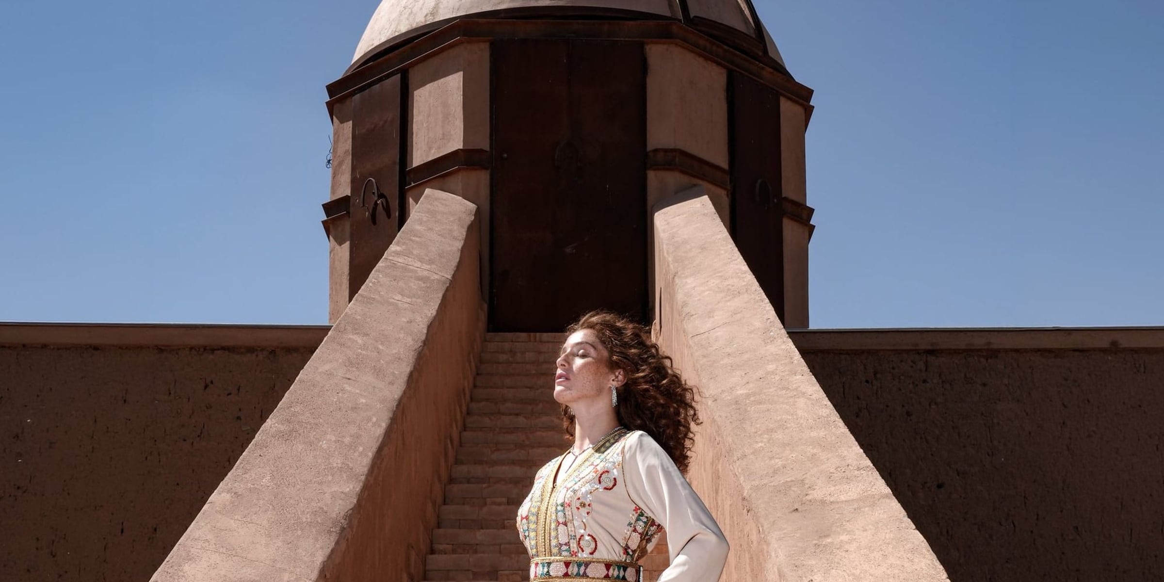 The red earth of Marrakech — Ecru Tapestry Moroccan kaftan on the steps of an adobe tower